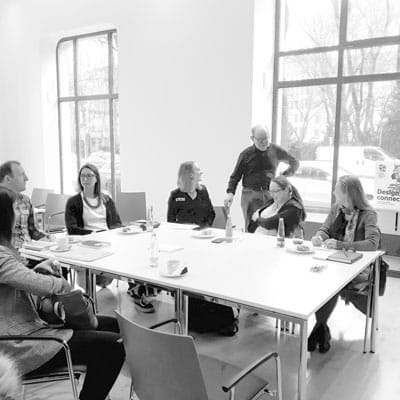 Kleingruppenarbeit beim Workshop Designmanagement: Teilnehmer sitzen am Tisch und der Workshopleiter Christhard Landgraf gibt freundliches Feedback